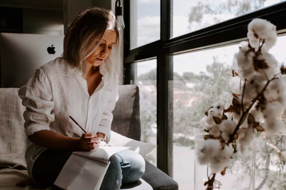 Woman sitting in front of window writing on a tablet