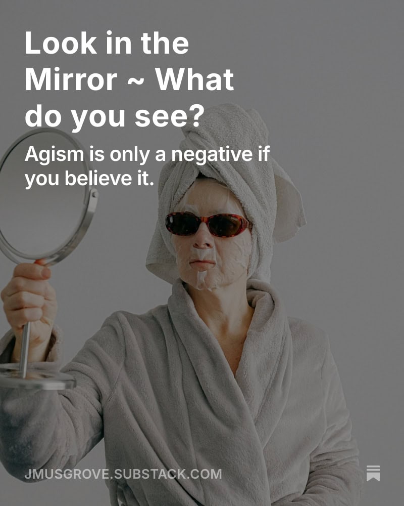 Woman in a robe looking in the mirror with a face mask and sunglasses on.